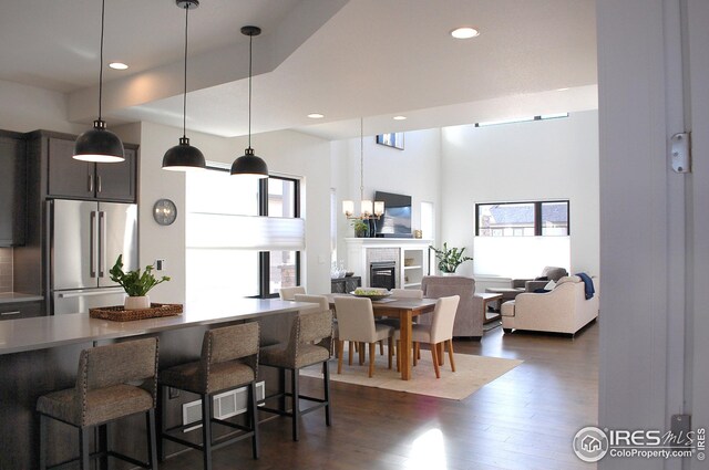 kitchen featuring a kitchen breakfast bar, decorative light fixtures, dark hardwood / wood-style floors, a towering ceiling, and high end fridge