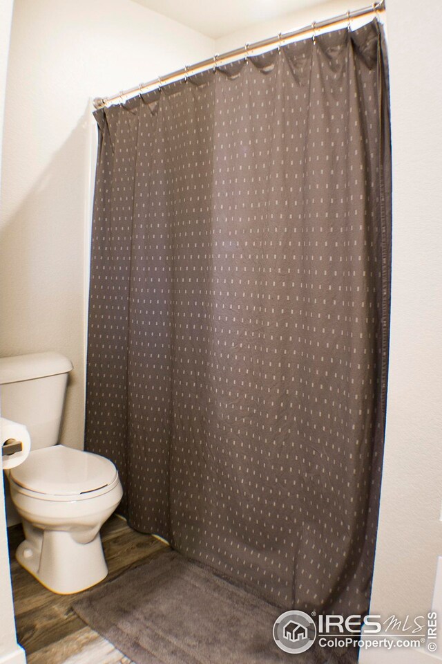 bathroom with hardwood / wood-style floors, toilet, and a shower with shower curtain