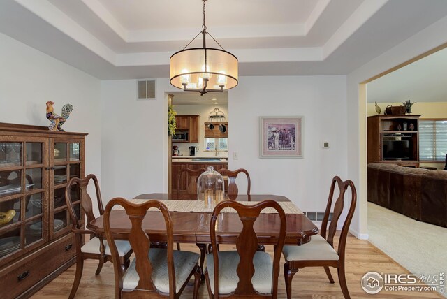 dining space featuring a tray ceiling, light hardwood / wood-style floors, and a notable chandelier