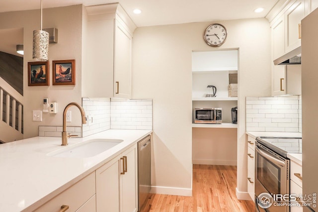 kitchen featuring decorative light fixtures, light wood finished floors, light countertops, appliances with stainless steel finishes, and a sink