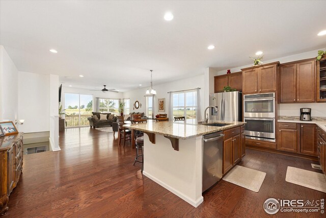 kitchen with a breakfast bar, dark wood-type flooring, a kitchen island with sink, ceiling fan with notable chandelier, and stainless steel appliances