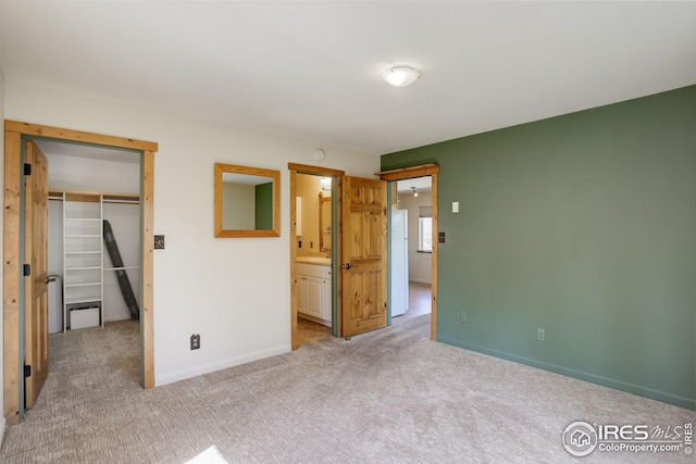 unfurnished bedroom with light colored carpet, white refrigerator, a closet, and ensuite bathroom