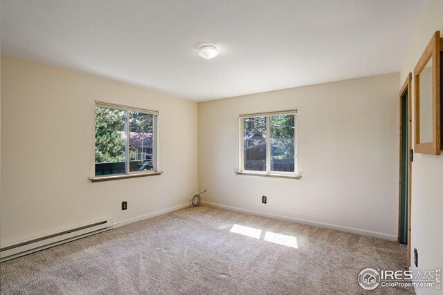 carpeted empty room featuring a baseboard heating unit and plenty of natural light