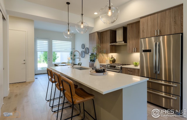 kitchen featuring a kitchen island with sink, a sink, stainless steel appliances, light countertops, and wall chimney exhaust hood