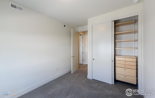 unfurnished bedroom with a closet, baseboards, visible vents, and dark colored carpet