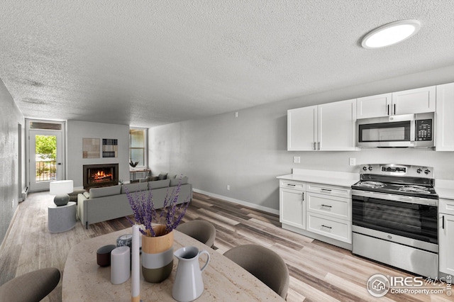 kitchen featuring a textured ceiling, stainless steel appliances, light hardwood / wood-style floors, and white cabinetry