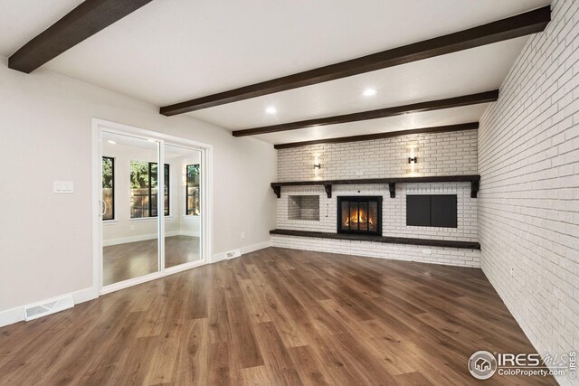 unfurnished living room with hardwood / wood-style flooring, a fireplace, beamed ceiling, and brick wall