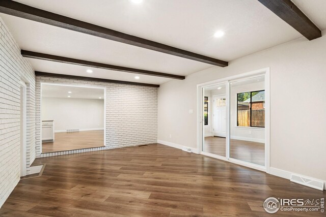 unfurnished living room with beam ceiling, brick wall, and dark wood-type flooring