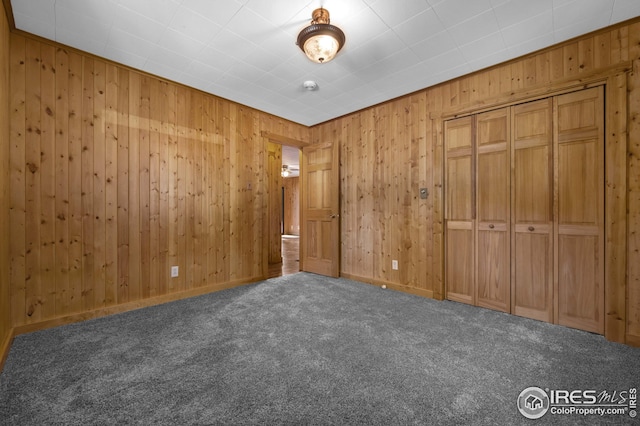 unfurnished bedroom with carpet floors, baseboards, a closet, and wood walls