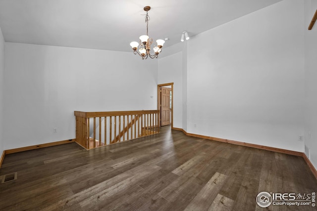empty room featuring baseboards, visible vents, wood finished floors, and a notable chandelier