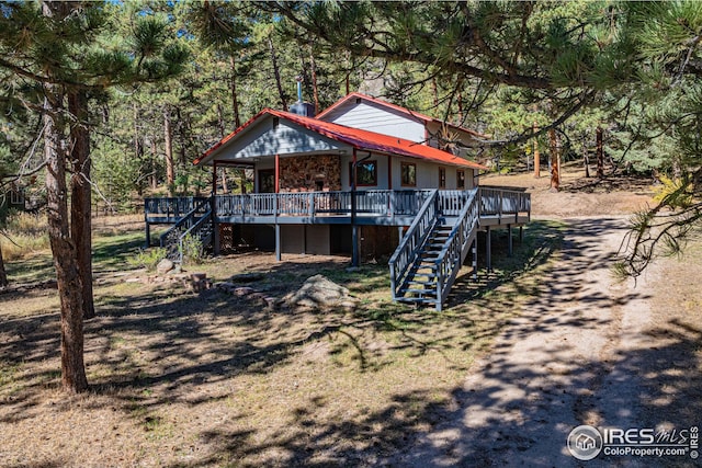 view of front facade featuring stairs, metal roof, a deck, and a forest view