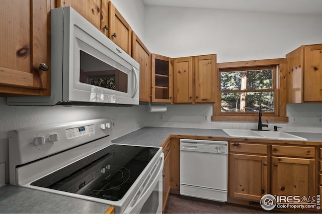 kitchen featuring brown cabinetry, a sink, and white appliances