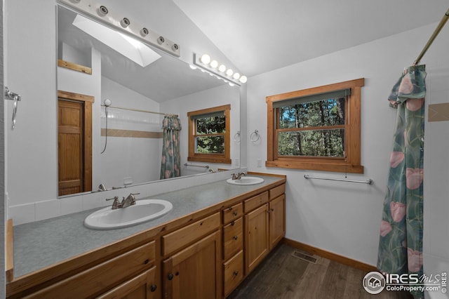 bathroom with visible vents, a sink, vaulted ceiling with skylight, and wood finished floors