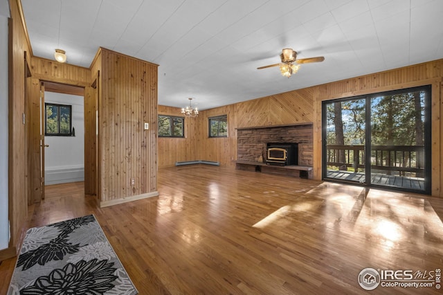 unfurnished living room with plenty of natural light, ceiling fan with notable chandelier, wood walls, and wood finished floors
