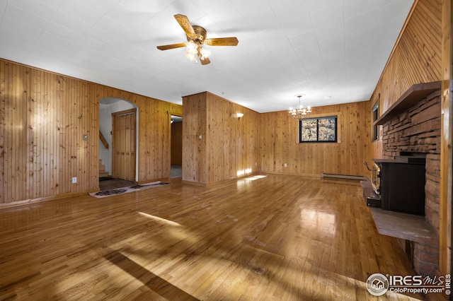 unfurnished living room featuring arched walkways, a baseboard radiator, ceiling fan with notable chandelier, and hardwood / wood-style floors