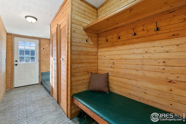 mudroom featuring a textured ceiling and wood walls