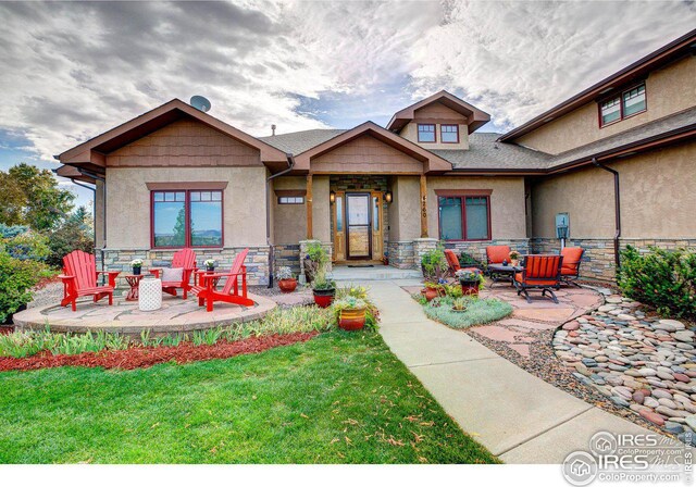 rear view of house featuring stone siding, a patio area, a yard, and stucco siding