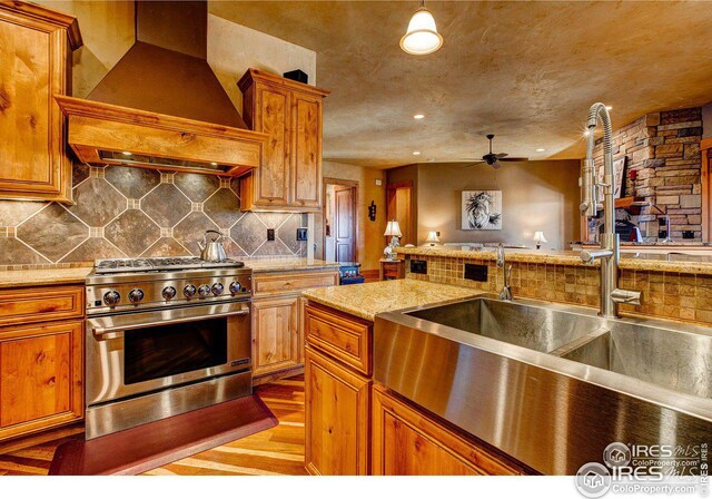 kitchen featuring brown cabinets, custom exhaust hood, high end stainless steel range oven, decorative backsplash, and a sink