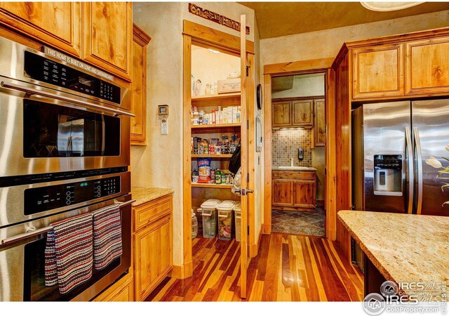 kitchen featuring light stone counters, light wood-style floors, appliances with stainless steel finishes, backsplash, and brown cabinets