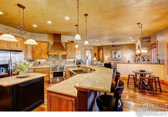 kitchen featuring stainless steel appliances, a sink, backsplash, wall chimney exhaust hood, and a center island with sink