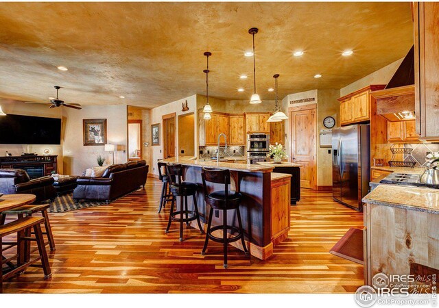 kitchen with stainless steel appliances, light wood-type flooring, open floor plan, and wall chimney range hood