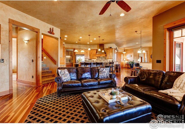 living room with baseboards, stairway, ceiling fan with notable chandelier, light wood-type flooring, and recessed lighting