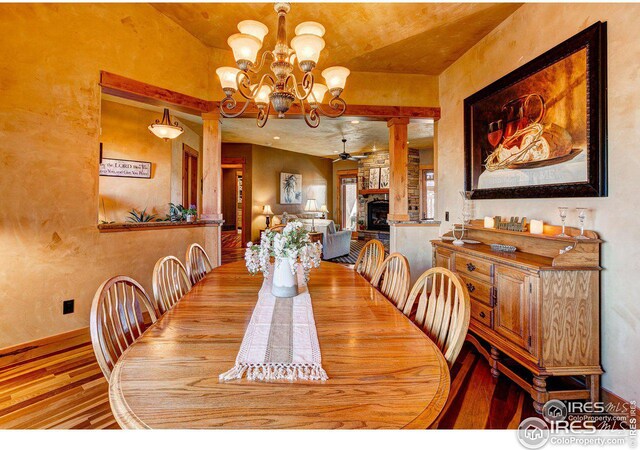 dining space with decorative columns, a fireplace, wood finished floors, and ceiling fan with notable chandelier