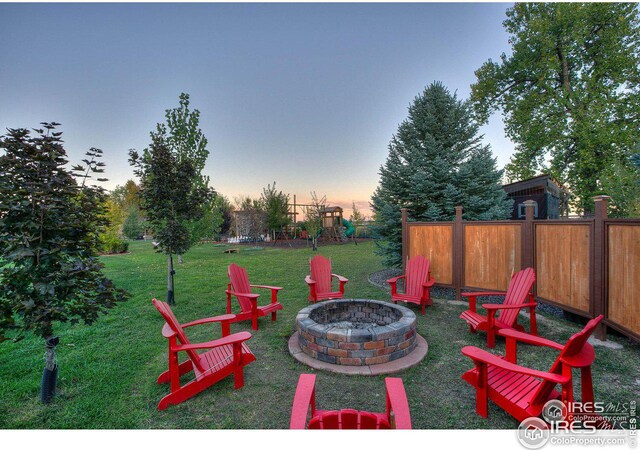 patio terrace at dusk with a fire pit, a yard, a playground, and fence