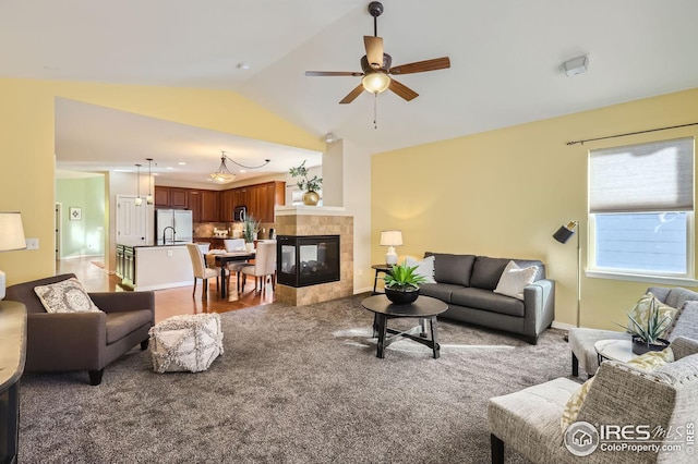 carpeted living room with ceiling fan, a tile fireplace, and vaulted ceiling