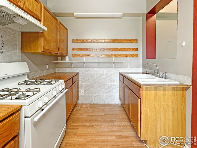 kitchen with brown cabinetry, light countertops, white range with gas cooktop, under cabinet range hood, and a sink