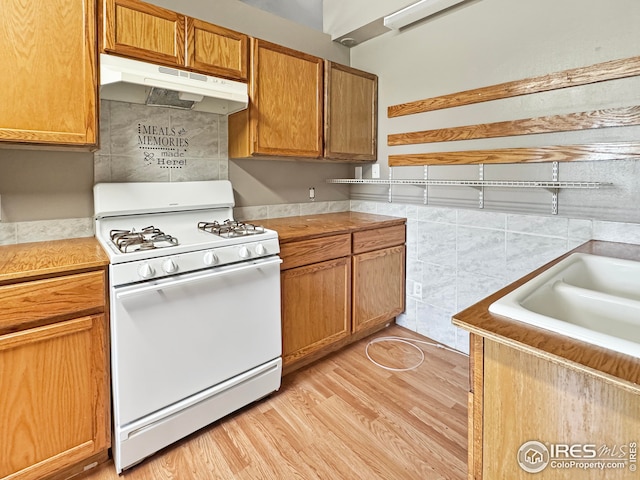 kitchen with gas range gas stove, light countertops, under cabinet range hood, brown cabinets, and light wood finished floors
