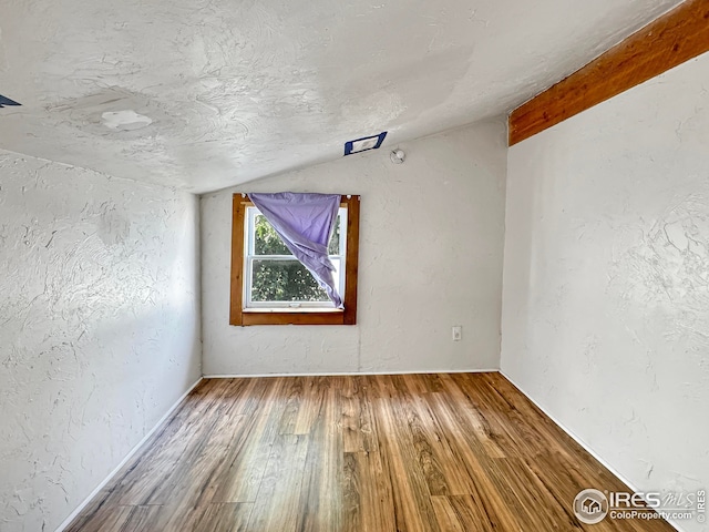 spare room with a textured wall, wood finished floors, and lofted ceiling