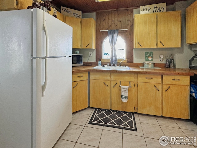 kitchen with a sink, wood ceiling, light tile patterned floors, and freestanding refrigerator