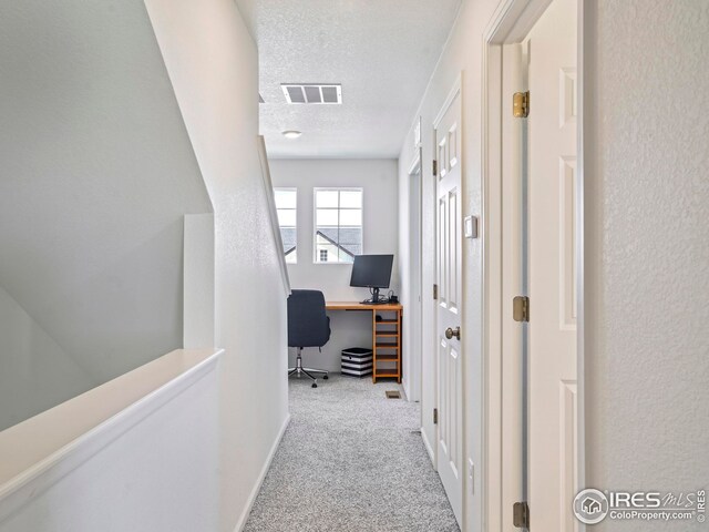 corridor featuring light carpet and a textured ceiling