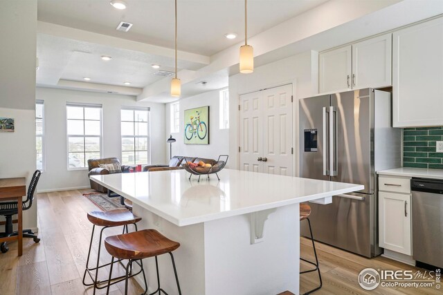 kitchen with appliances with stainless steel finishes, light hardwood / wood-style floors, white cabinetry, a raised ceiling, and a kitchen bar