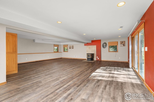 unfurnished living room with hardwood / wood-style floors, a healthy amount of sunlight, a wood stove, and beamed ceiling