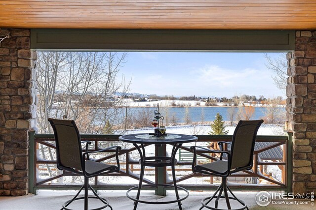 snow covered patio featuring a balcony and a water view