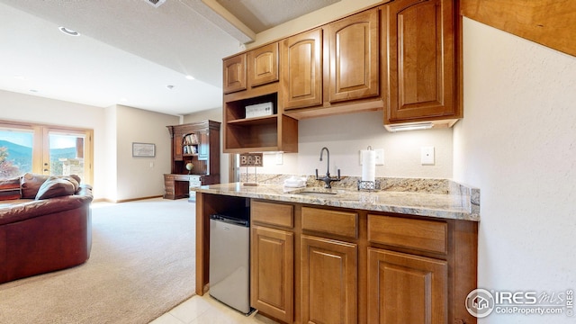 kitchen featuring light stone counters, light colored carpet, a textured ceiling, and sink