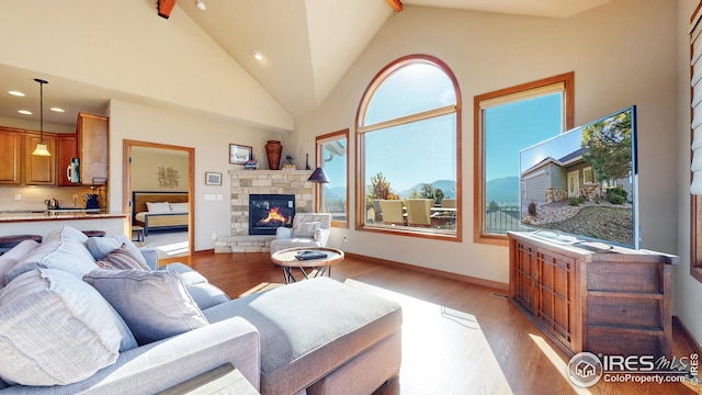 living room with beamed ceiling, a fireplace, light hardwood / wood-style floors, and high vaulted ceiling