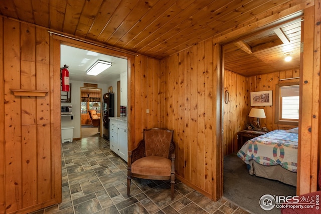 bedroom featuring freestanding refrigerator, wood ceiling, stone finish floor, and wooden walls