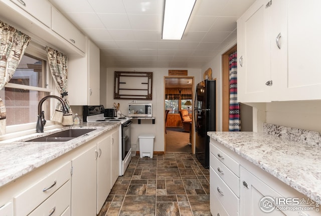 kitchen featuring electric range, stainless steel microwave, freestanding refrigerator, white cabinetry, and a sink