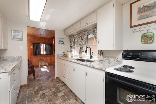 kitchen with a sink, stone finish flooring, white cabinetry, and electric stove