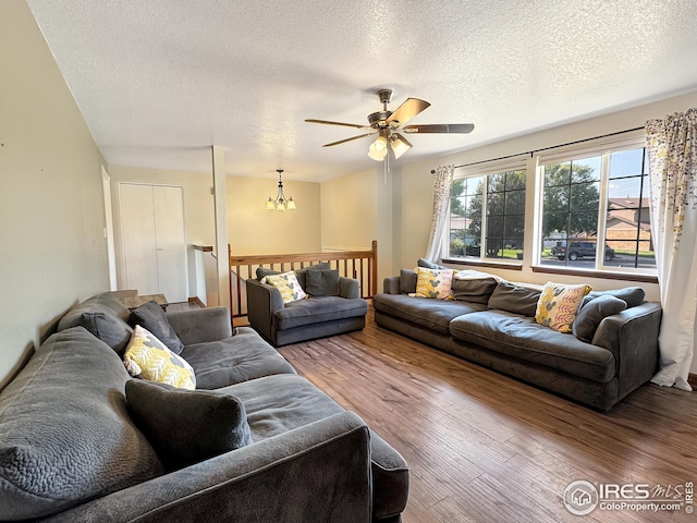 living room with wood-type flooring, ceiling fan with notable chandelier, and a textured ceiling