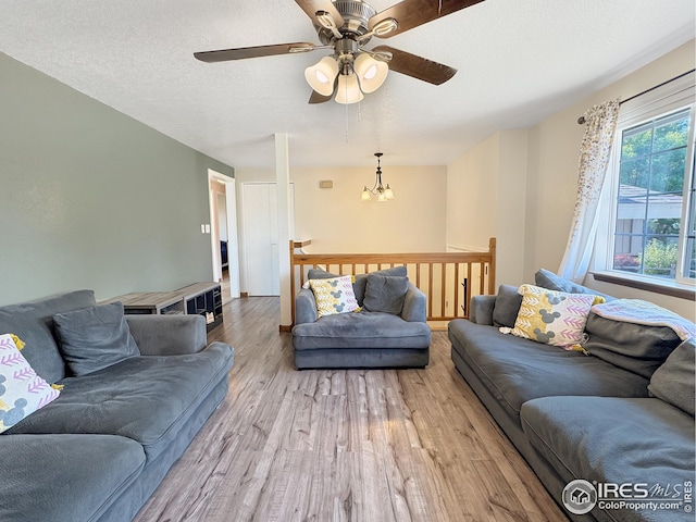 living room featuring ceiling fan with notable chandelier, light hardwood / wood-style floors, and a textured ceiling