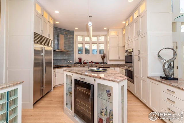 kitchen with wall chimney range hood, light wood-style floors, stainless steel appliances, recessed lighting, and wine cooler