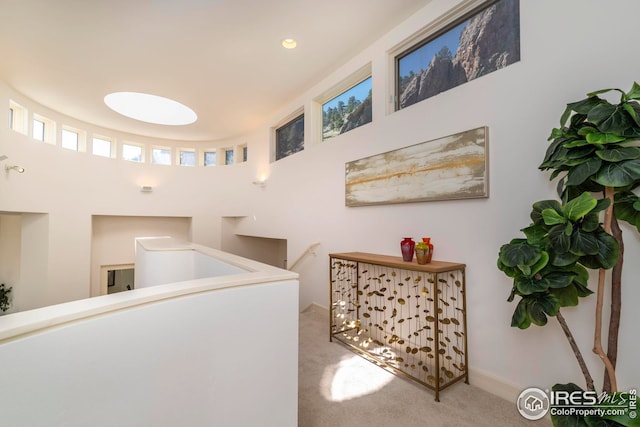 hall featuring an upstairs landing, a towering ceiling, baseboards, and carpet floors