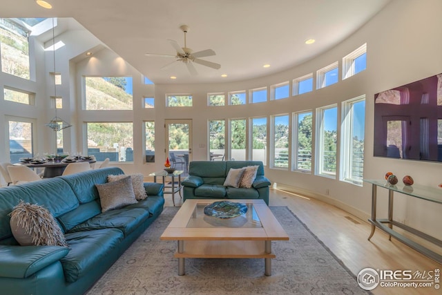 living room featuring a ceiling fan, wood finished floors, a healthy amount of sunlight, and a towering ceiling