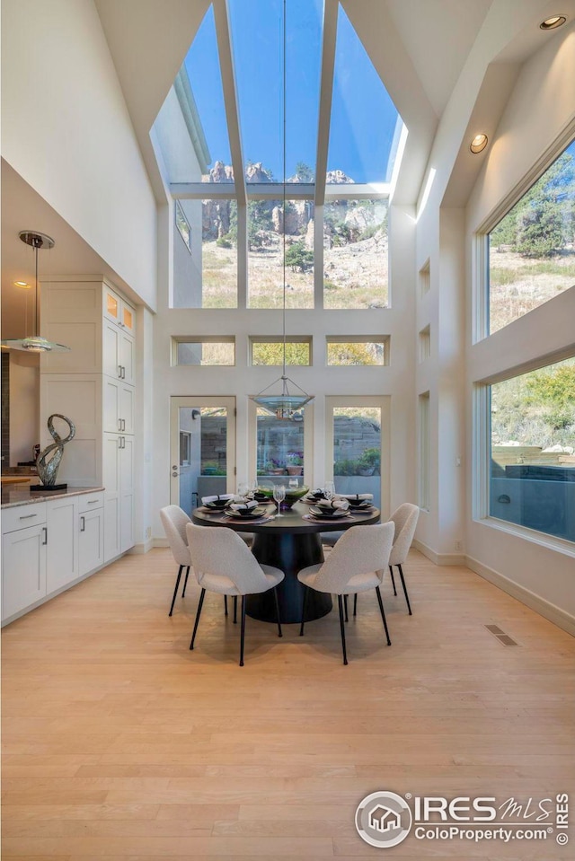 dining room with baseboards, light wood-type flooring, and a high ceiling