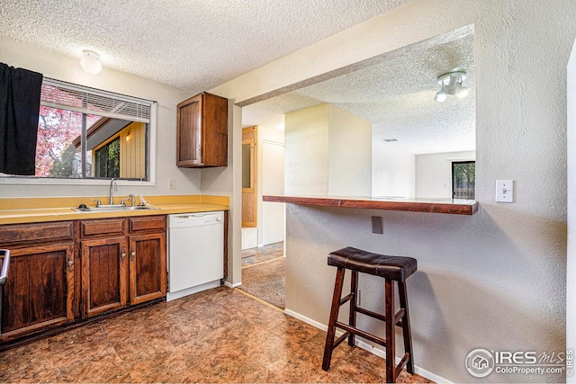 kitchen with a breakfast bar, sink, dishwasher, kitchen peninsula, and a textured ceiling