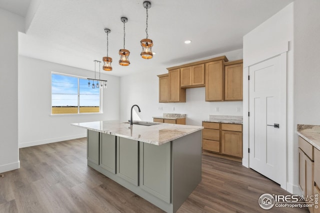 kitchen featuring light stone countertops, dark wood finished floors, an island with sink, a sink, and brown cabinets